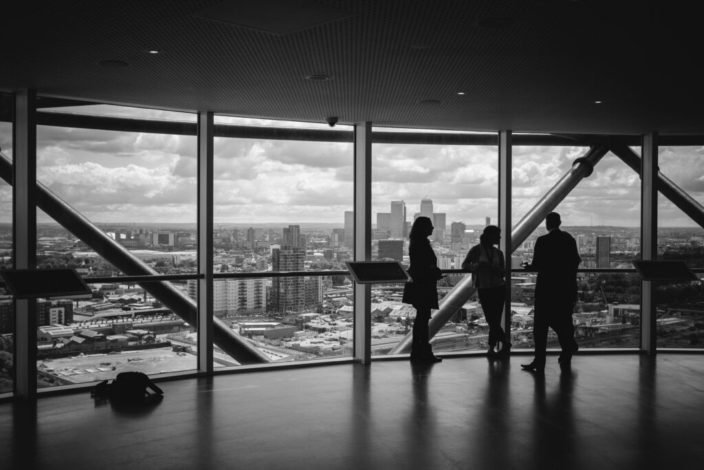 People silhouetted against floor-to-ceiling windows overlooking a city