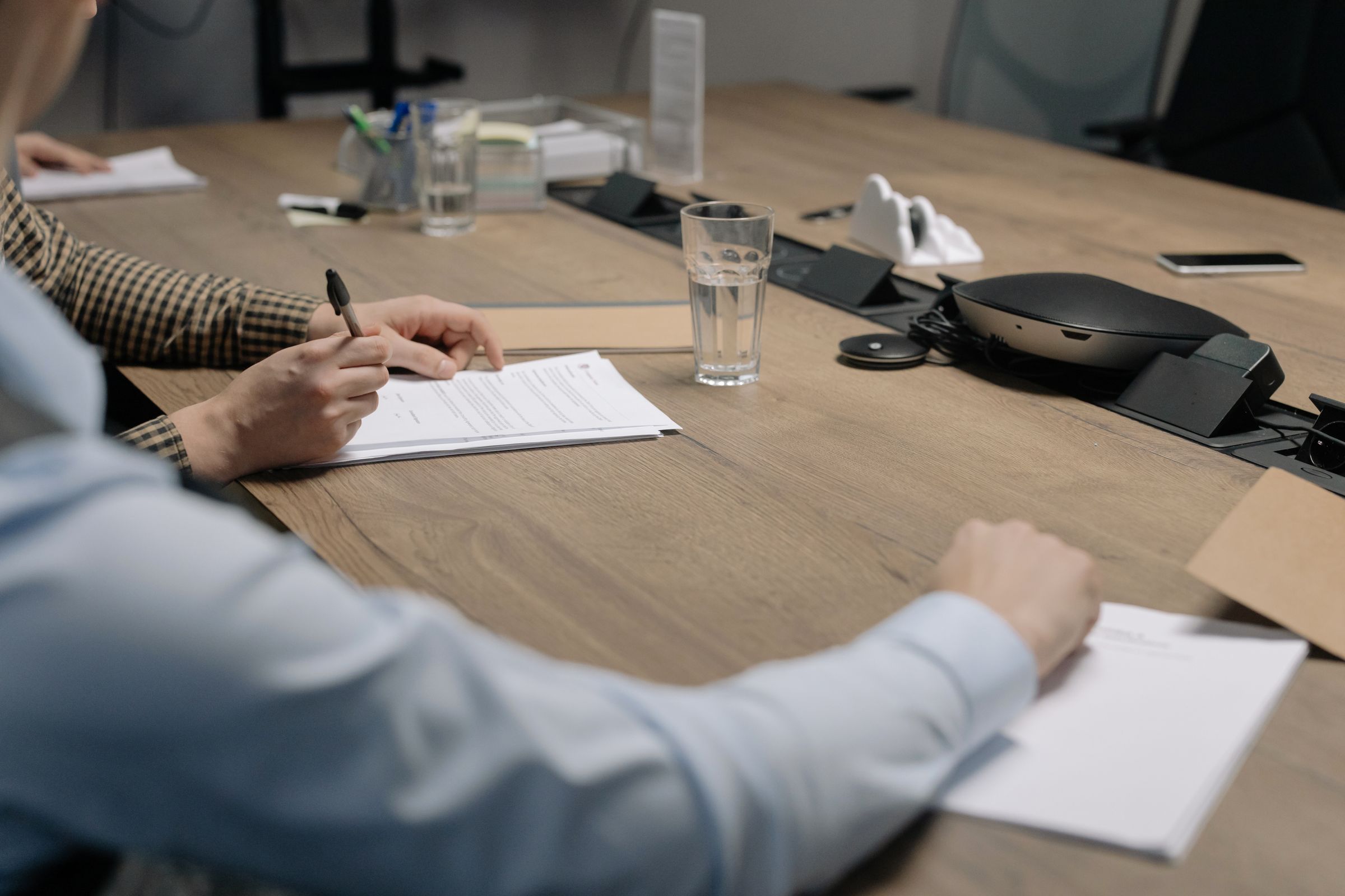 Committee members reviewing and signing papers at a boardroom table with a conference phone